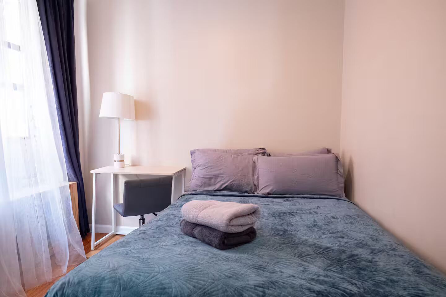 A bedroom with a bed, a bedside table, a lamp, and a window with curtains.