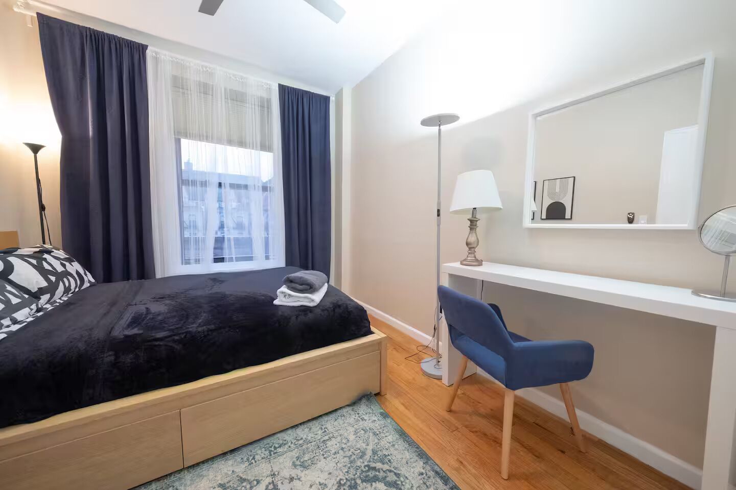 Un dormitorio con cama, escritorio, silla, lámpara y ventana con cortinas.
