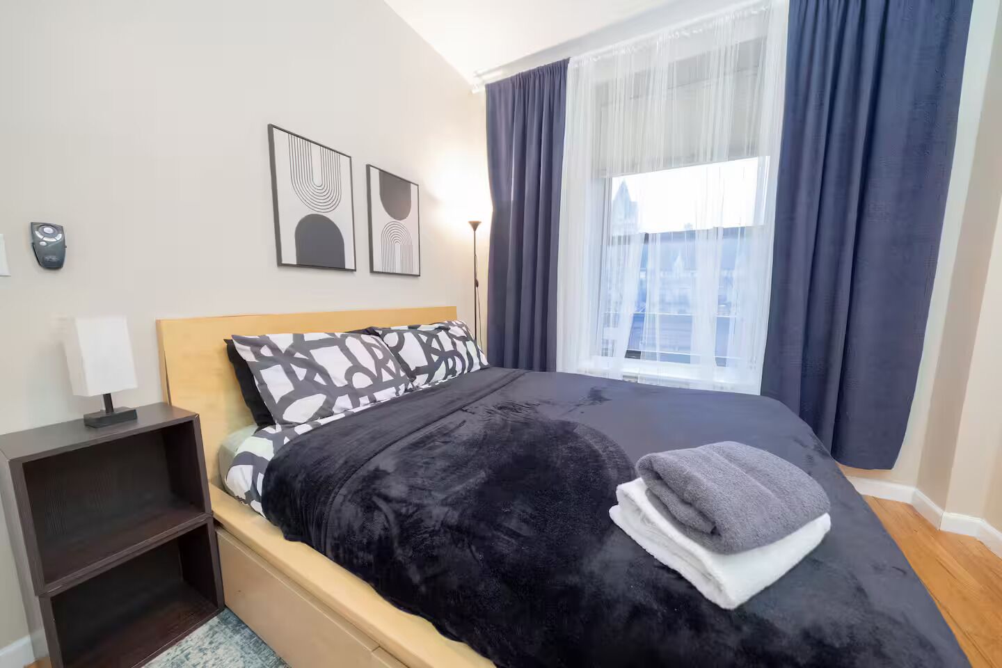 Een moderne hotelkamer met een groot bed, een nachtkastje met een lamp en een raam met gordijnen.