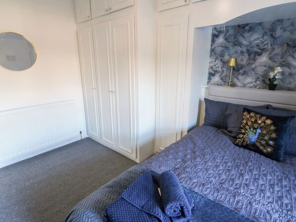 A bedroom with a bed, a wardrobe, a mirror, and a marble wall. - 16 Salvin Terrace (Stockton-on-Tees)