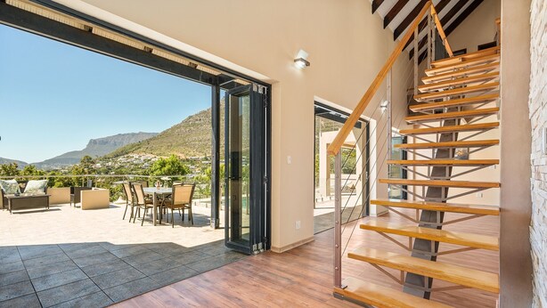 Eine geräumige Terrasse mit Gartenmöbeln, einer Holztreppe und einer Glastür zu einem schönen Ausblick.