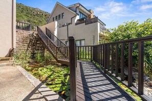 Een modern gebouw met een trap die naar een balkon leidt, omgeven door groen en een houten terras.