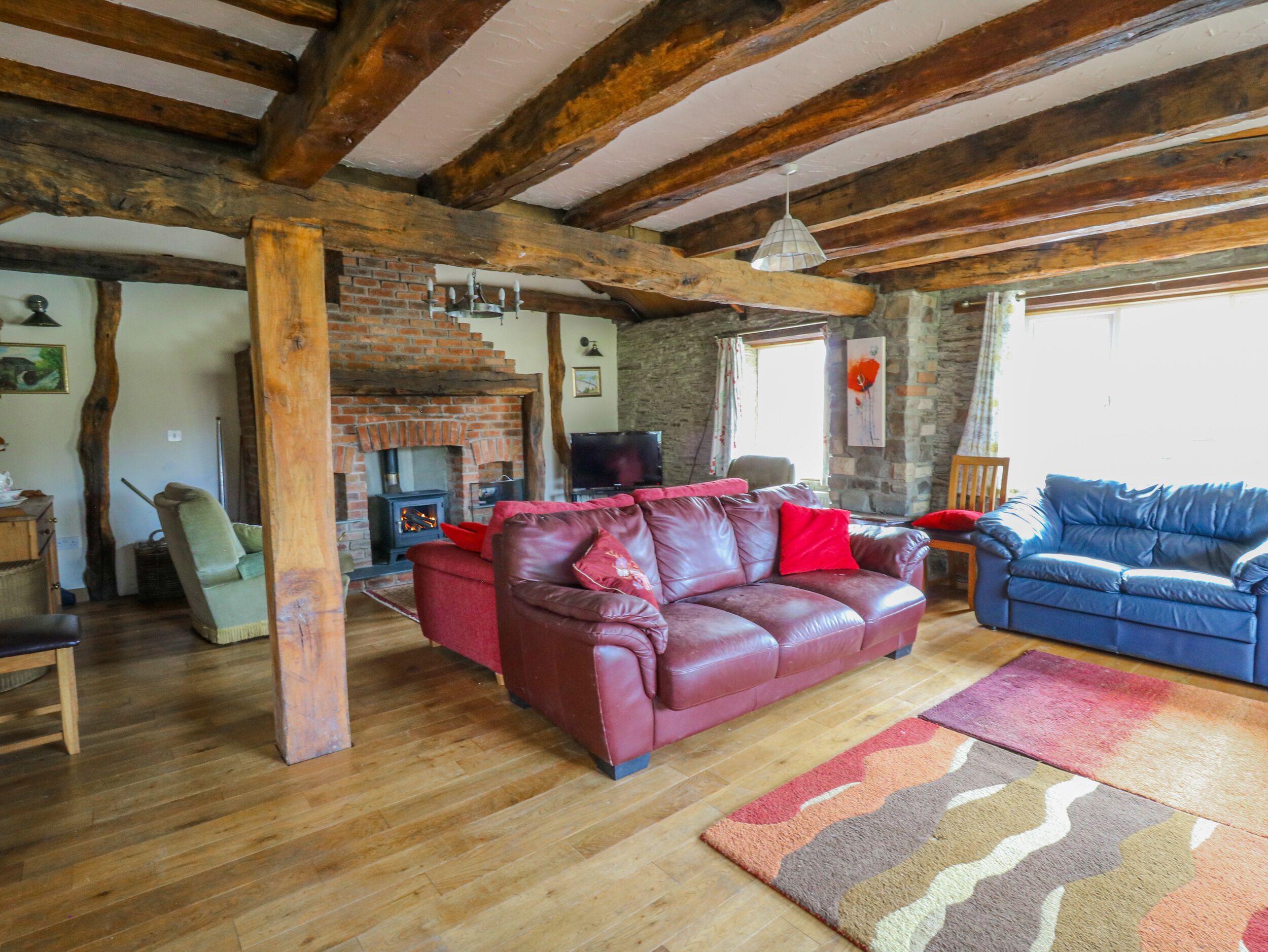 Ein rustikales Wohnzimmer mit sichtbaren Holzbalken, einem Kamin aus Ziegelsteinen, Ledersofas und einem Fernseher.