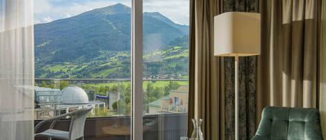 A room with a view of a mountain, a table with glasses, a chair, and a lamp.