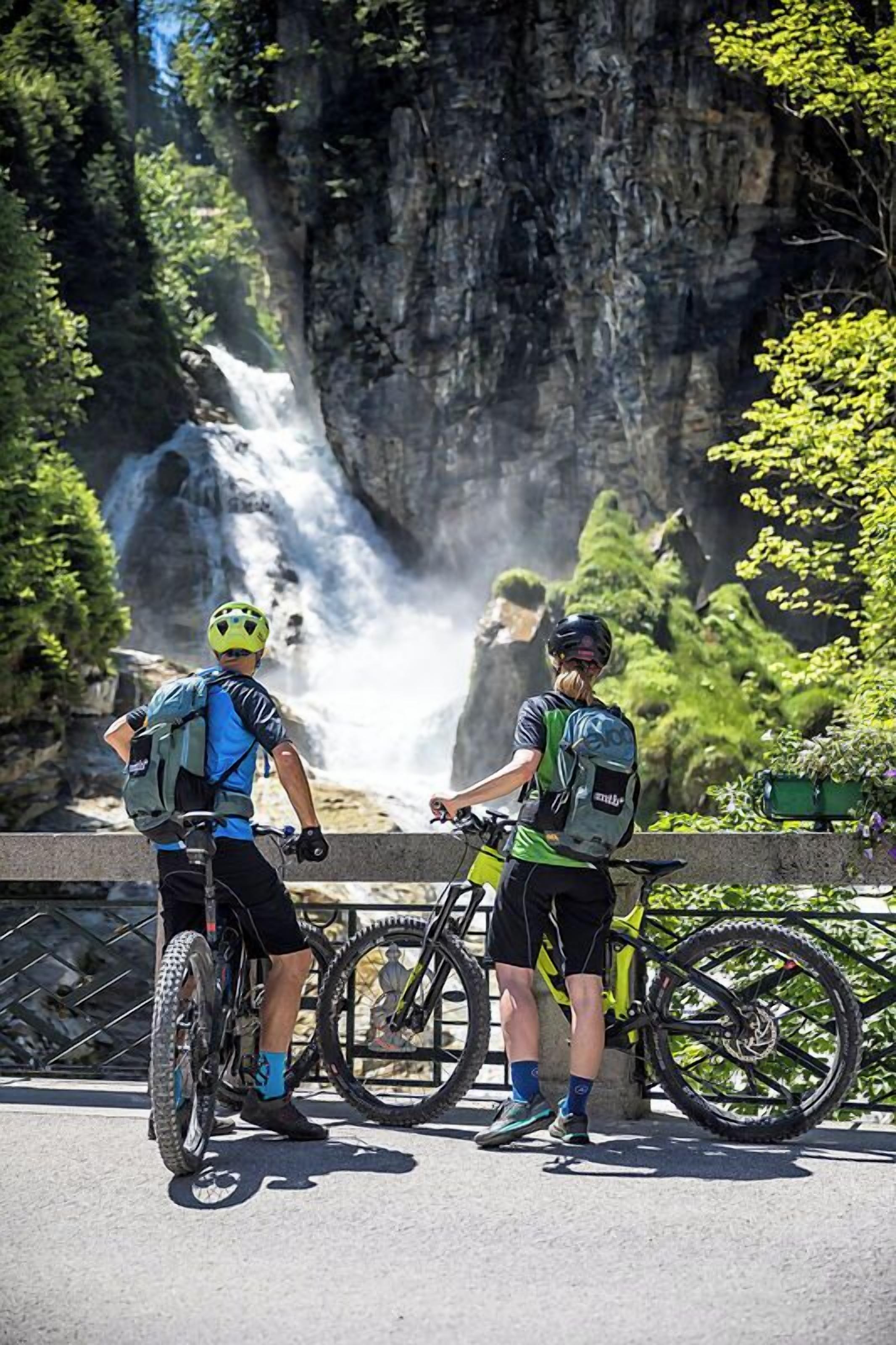 Two cyclists with bicycles near a waterfall.