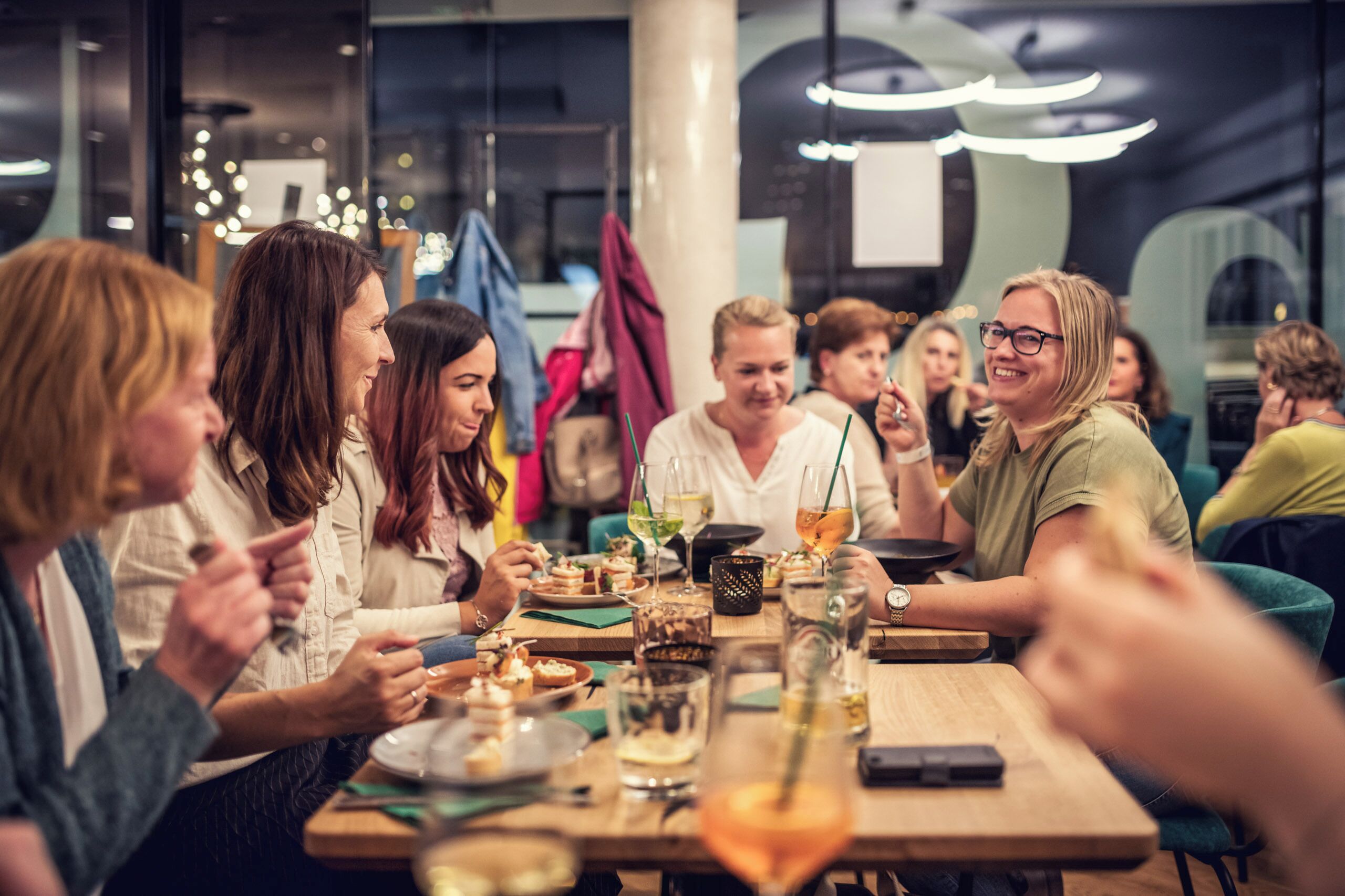 Een groep mensen dineert in een restaurant met een modern interieur, inclusief een houten tafel en eigentijdse verlichtingsarmaturen.