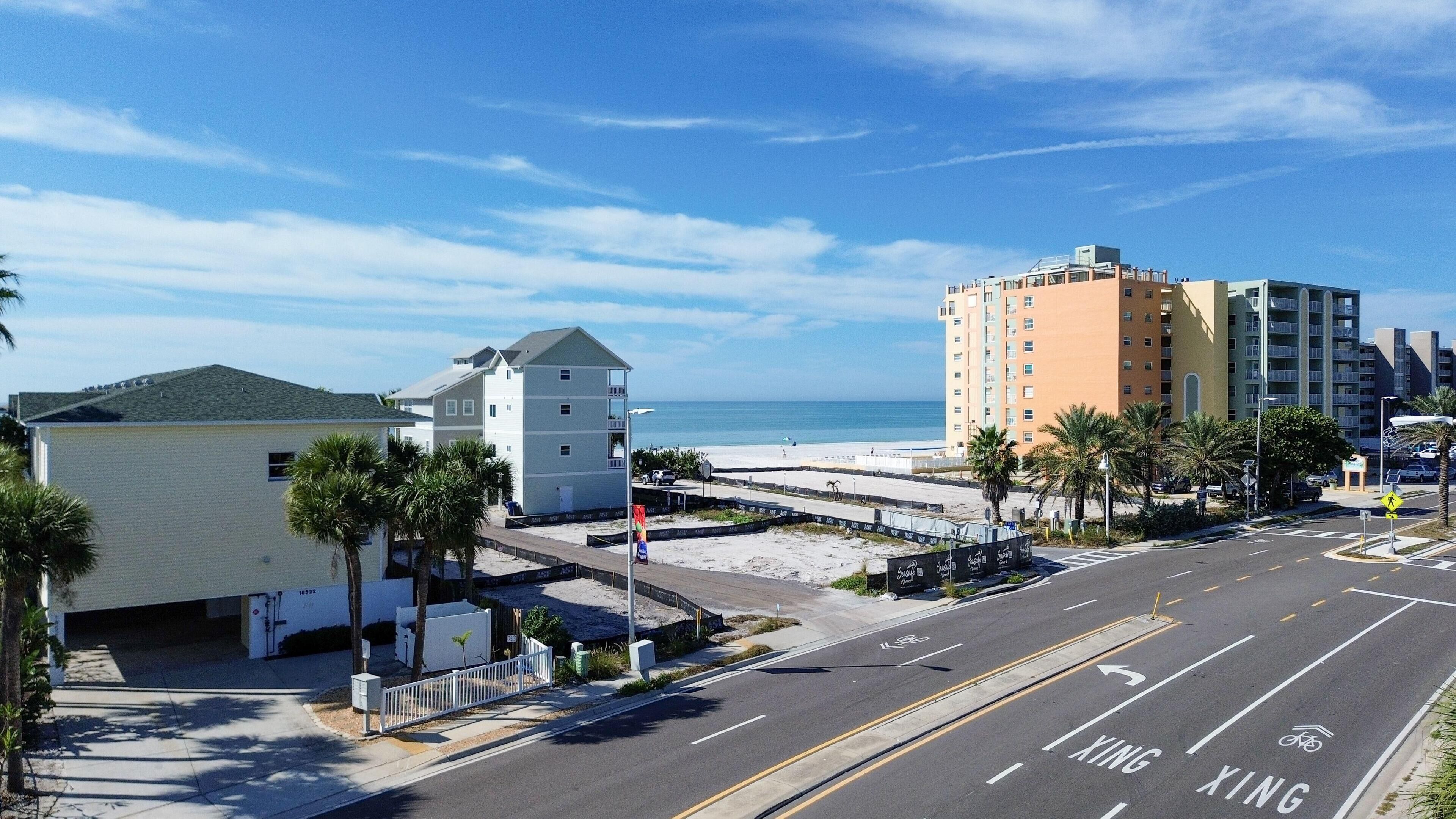 A coastal road with a pedestrian crossing, a beach, and buildings including a multi-story hotel.