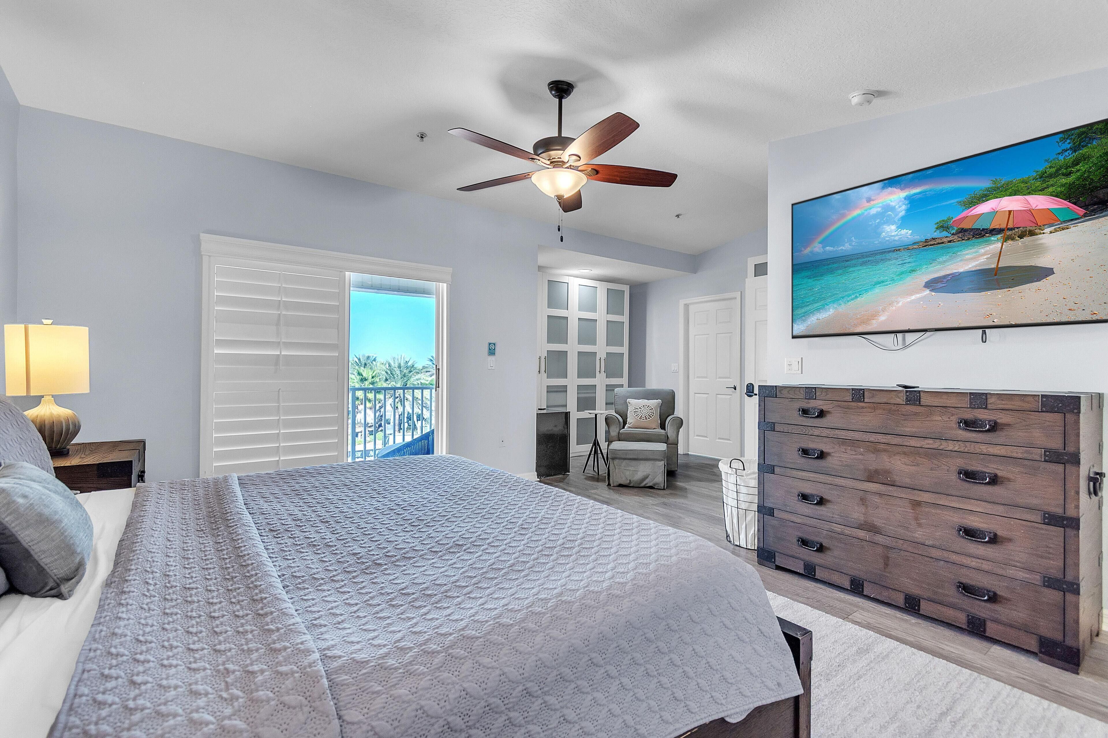 A bedroom with a bed, a ceiling fan, a TV, and a dresser.