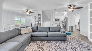 A modern living room with a grey sectional sofa, a patterned rug, and ceiling fans. - El Mar Townhome - Unit D (Indian Shores)