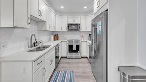 A modern kitchen with white cabinetry, stainless steel appliances, and a central island. - El Mar Townhome - Unit D (Indian Shores)