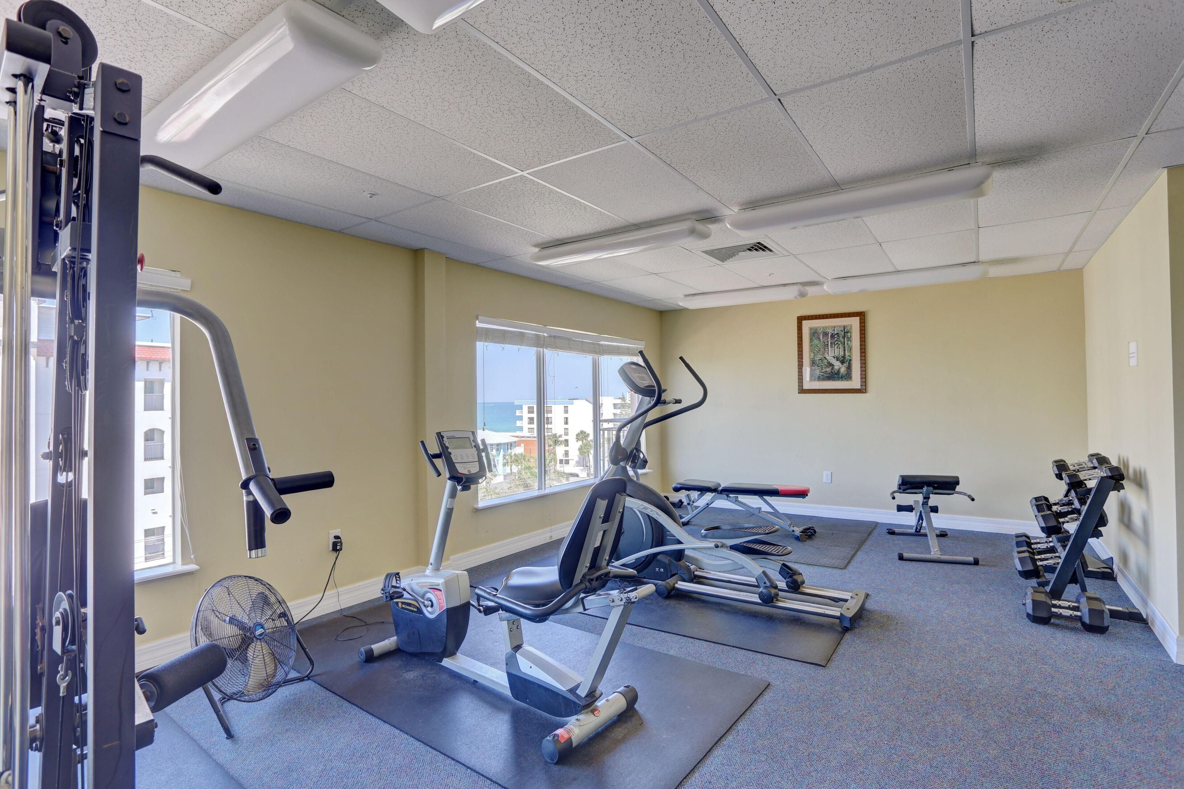 A gym with exercise equipment, a fan, and a window with a view of buildings.