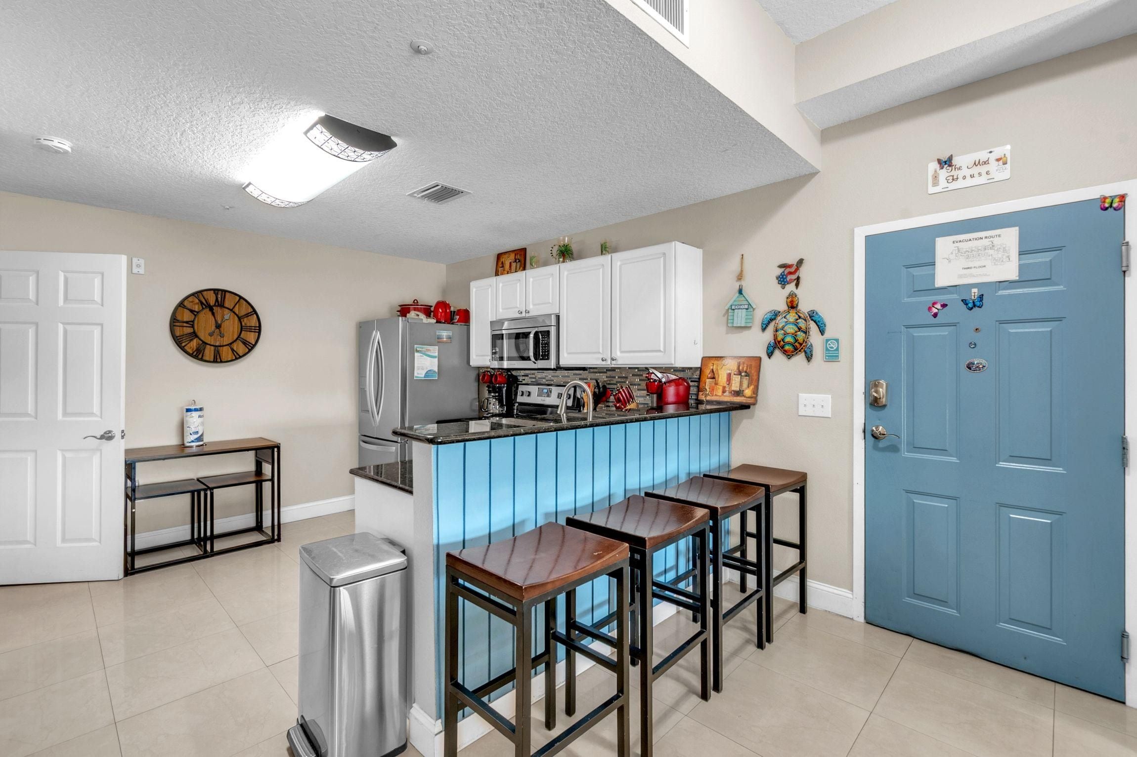 Una cocina moderna con una barra azul, armarios blancos y un refrigerador de acero inoxidable.