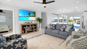 A modern living room with a grey sofa, starfish-patterned armchairs, a flat-screen TV, and a ceiling fan.
