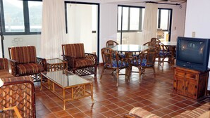 Un salón espacioso con mobiliario de mimbre, una mesa de centro de vidrio y un televisor.