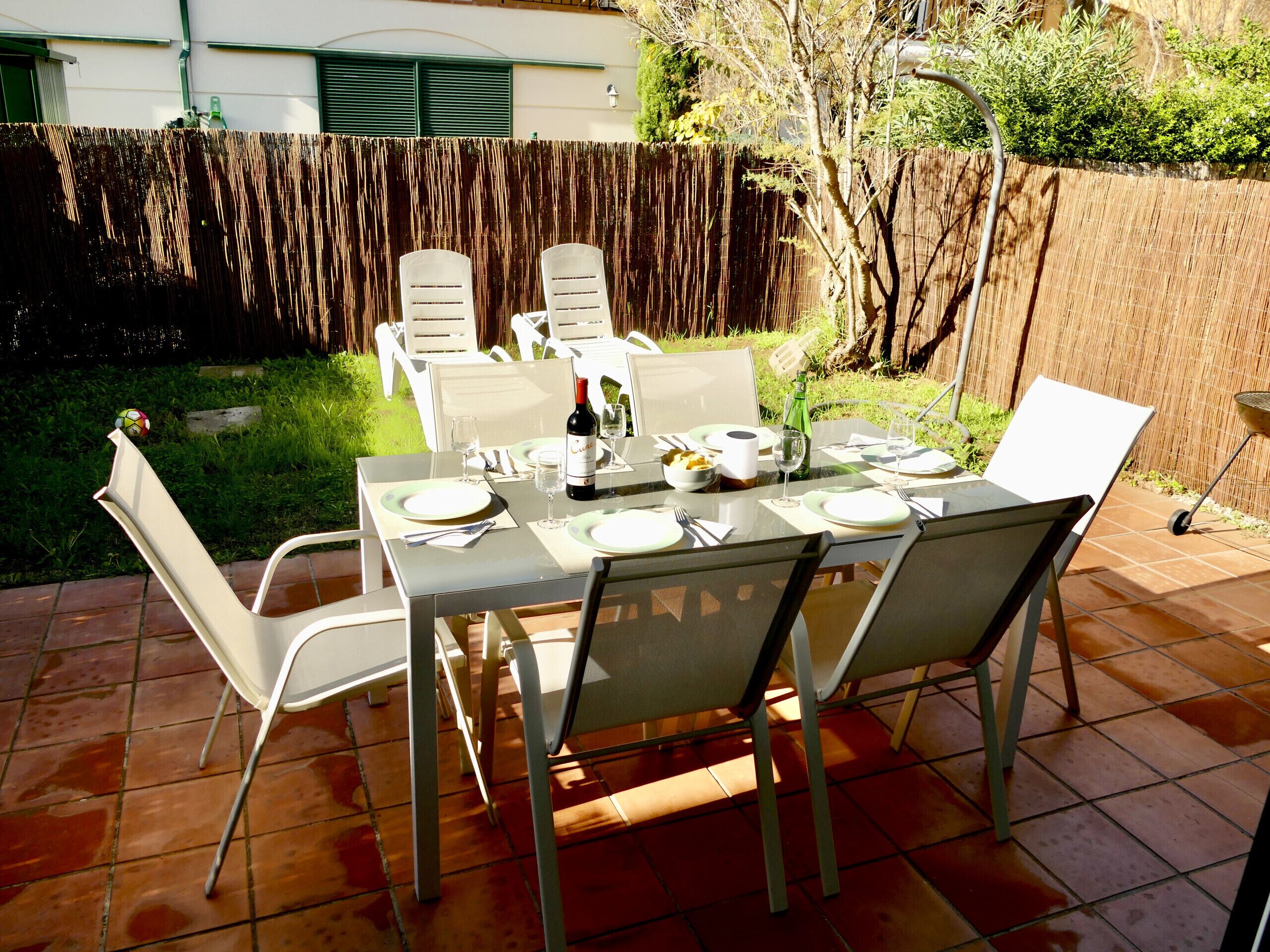 Een buitenterras met een tafel voor vier personen, omringd door stoelen, en een barbecue op de achtergrond.