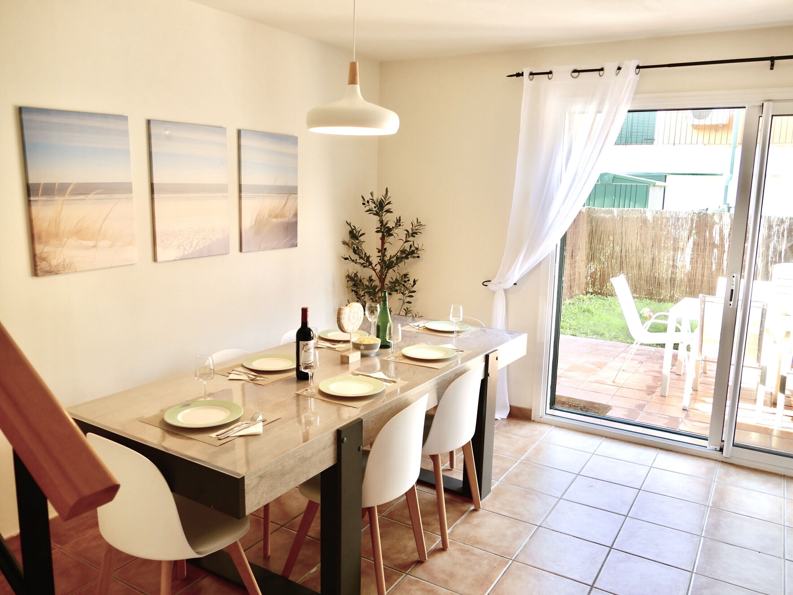 A dining area with a table set for four, a bottle of wine, and a vase of greenery.