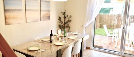 A dining area with a table set for four, a bottle of wine, and a vase of greenery.