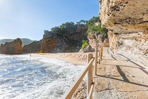 Una passeggiata costiera con ringhiera in legno che conduce a una spiaggia, con onde e scogliere rocciose sullo sfondo.