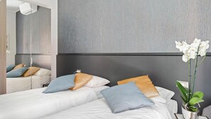 Une chambre d’hôtel avec deux lits, un grand miroir, une orchidée en pot et un décor moderne.