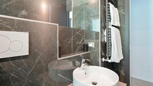 Une salle de bain moderne avec un lavabo rond, une cabine de douche en verre et un mur recouvert de carreaux de marbre.
