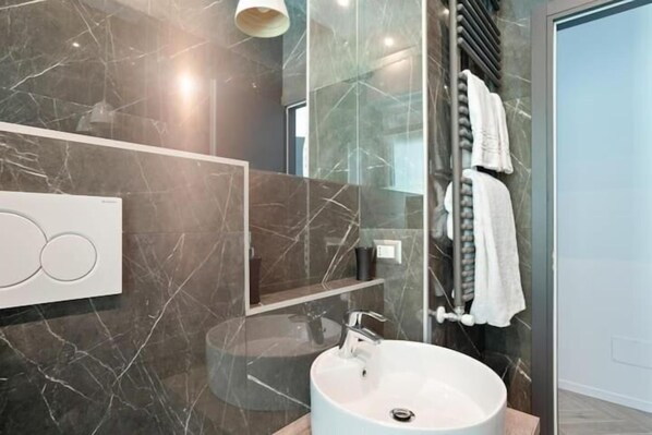 Un baño moderno con un lavabo redondo, cabina de ducha con paredes de vidrio y pared con azulejos de mármol.