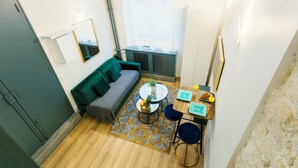 A compact living space with a sofa, a small round table with a plant and fruit, a chair, and a window with sheer curtains. - Charming Studio Near Madeleine (Paris)