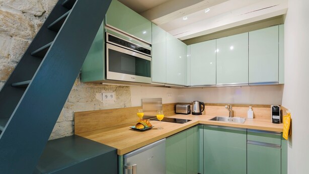 A modern kitchen with green cabinets, a built-in oven, a sink, and a coffee maker. - Charming Studio Near Madeleine (Paris)