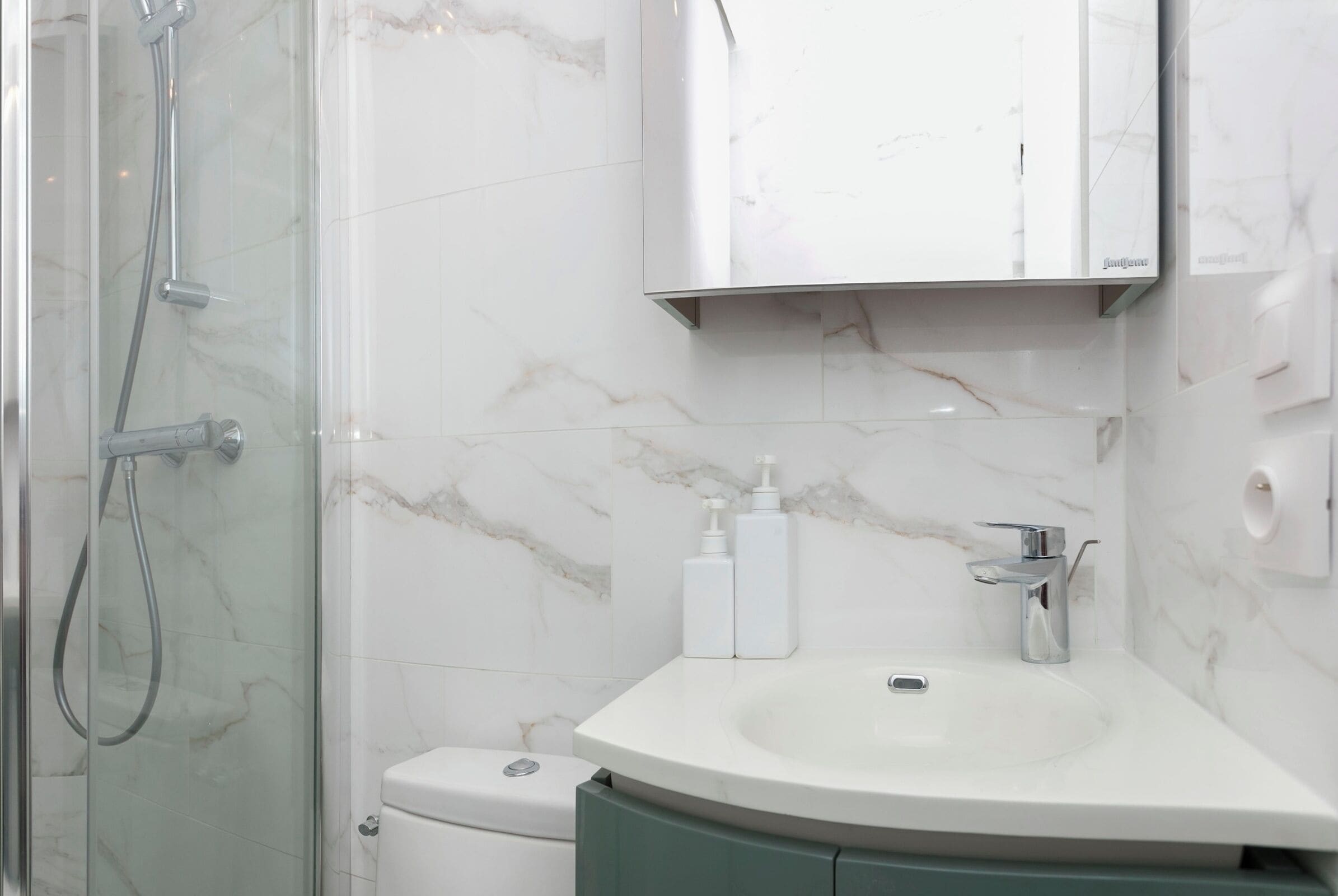 Een badkamer met een douchecabine van glas, een toilet, een wastafel met spiegel erboven en twee flessen toiletartikelen.