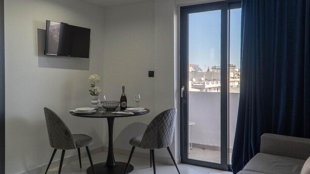 A modern dining area with a round table, two chairs, a flat-screen TV mounted on the wall, and a sliding glass door leading to an outdoor balcony. - Apartment 'Deluxe' with Sea View, Wi-Fi and Air Conditioning (Ρόδος)