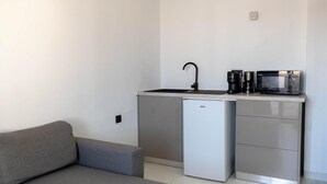 A compact kitchenette with a sink, microwave, and refrigerator, adjacent to a gray sofa. - Apartment 'Deluxe' with Sea View, Wi-Fi and Air Conditioning (Ρόδος)