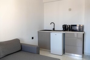 Eine kleine Küchenzeile mit Spüle, Mikrowelle und Kühlschrank, neben einem grauen Sofa.