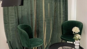 A room with a green curtain, a television screen displaying 'JVC Netflix,' two green chairs, a small round table, and a vase with white flowers. - Apartment 'Double Room Mountain View' with Sea View, Wi-Fi and Air Conditioning (Ρόδος)