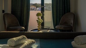 A hotel room with a bed, two chairs, a small table with a plant, a TV mounted on the wall, and a view through the window. - Apartment 'Double Room Mountain View' with Sea View, Wi-Fi and Air Conditioning (Ρόδος)