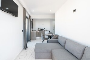 A modern living room with a grey sofa, a flat-screen TV mounted on the wall, a dining area with a table and chairs, and a kitchen in the background. - Apartment 'One-Bedroom' with Sea View, Wi-Fi and Air Conditioning (Ρόδος)
