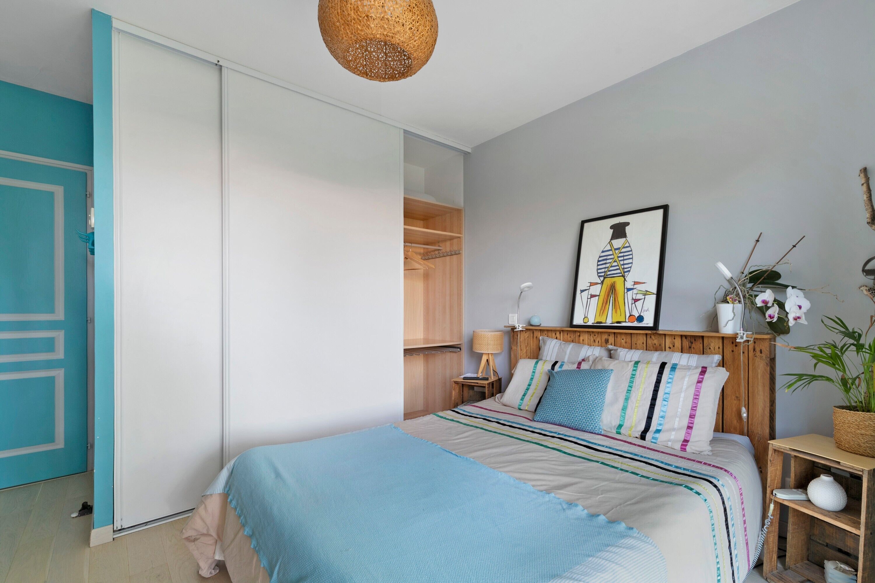 Een slaapkamer met een bed, een kledingkast, een nachtkastje, een lamp, een ingelijst kunstwerk en een potplant.