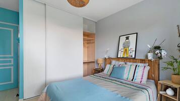 Een slaapkamer met een bed, een kledingkast, een nachtkastje, een lamp, een ingelijst kunstwerk en een potplant.