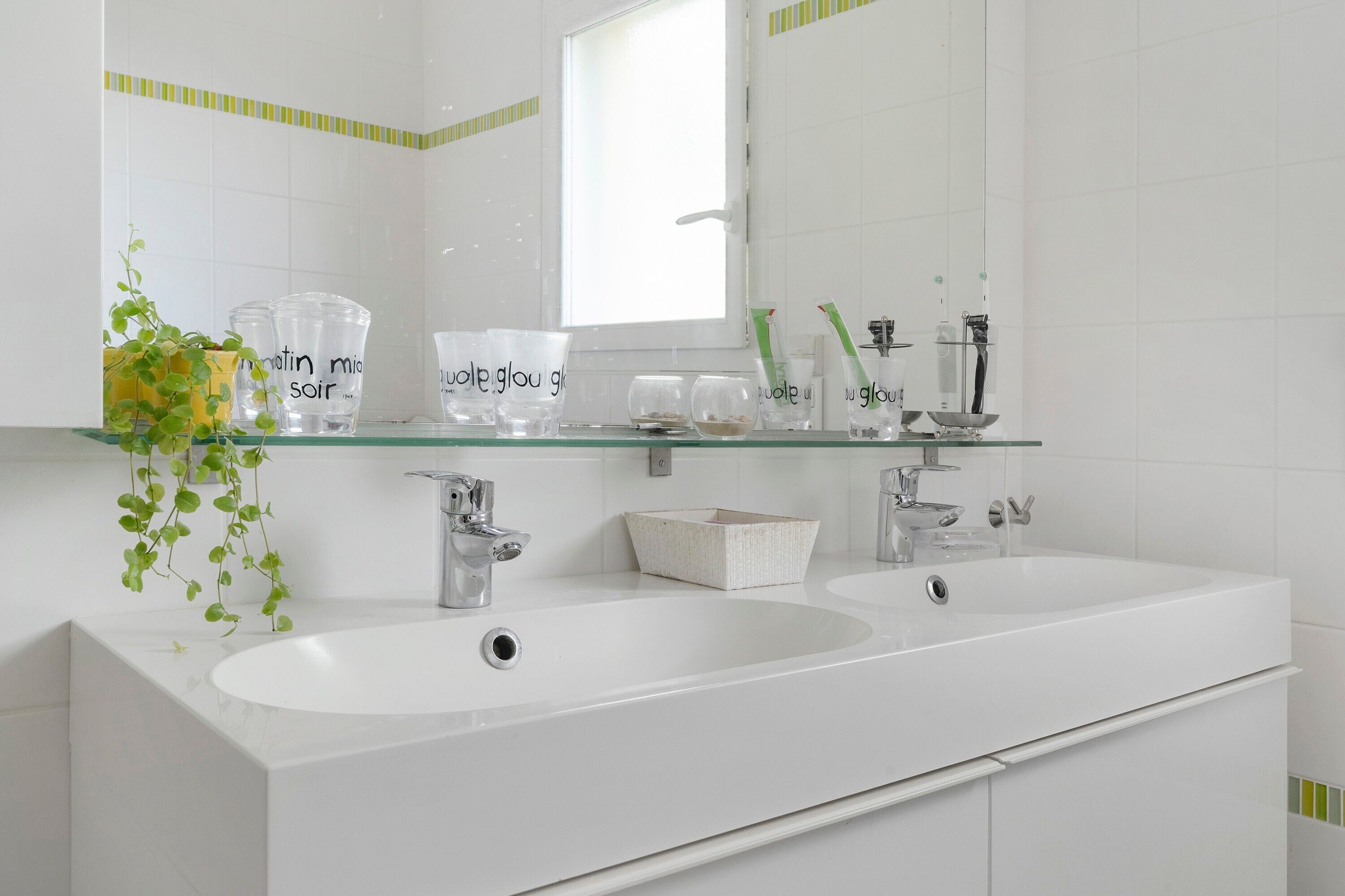 Une salle de bain moderne avec deux lavabos, un miroir et une étagère contenant des articles de toilette.