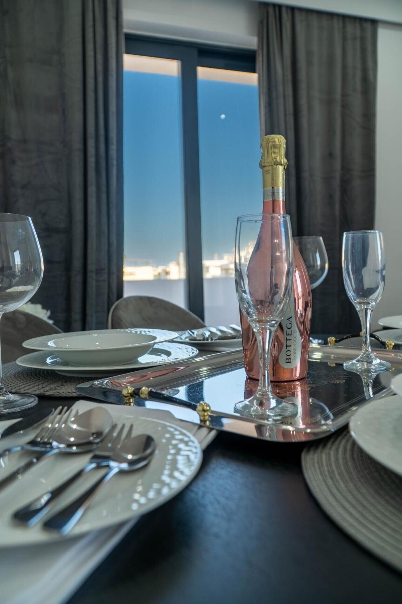 Una mesa de comedor lista con platos, cubiertos y vasos, con una botella de vino Bottega en el centro.