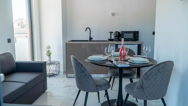 Ein modernes Wohnzimmer mit einer Couch, einem Esstisch für zwei Personen und einer Küche im Hintergrund.