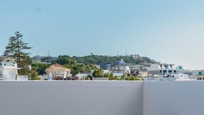Eine Dachterrasse mit einer weißen Blumenvase, einem runden Tisch und Blick auf Gebäude sowie einen Hügel in der Ferne.