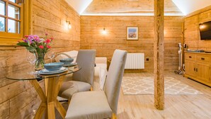 Interior acogedor de una cabaña de madera con comedor que incluye una mesa de vidrio, sillas y un florero con flores.