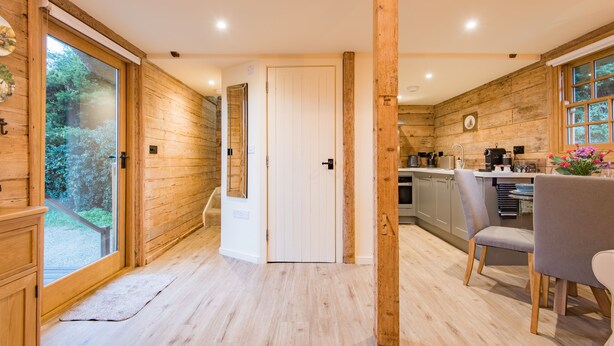 Un interior de madera con una zona de cocina, una mesa de comedor con sillas y una puerta que da a un espacio al aire libre.