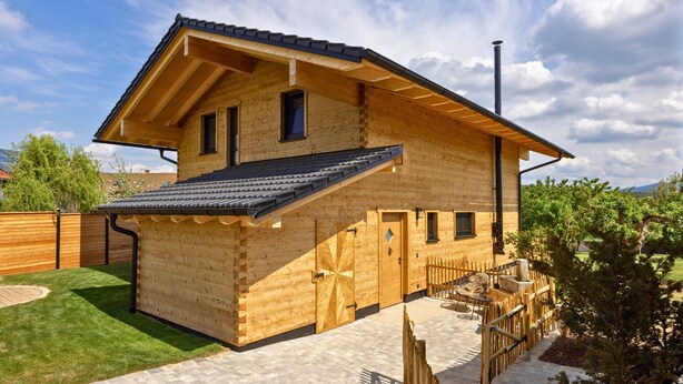 Una casa di legno con tetto spiovente, un camino e un cortile recintato.