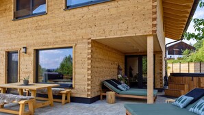 Facciata in legno con ampie finestre, posti a sedere all'aperto e una veranda coperta.