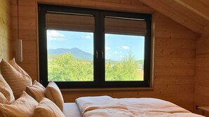 Una stanza con un letto, cuscini e un'ampia finestra vista verde e montagne.