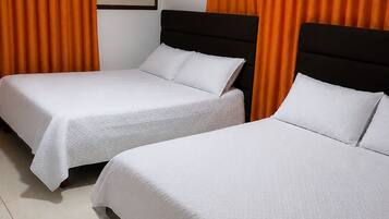 Quarto de hotel com duas camas de solteiro, cortinas laranja, um quadro emoldurado na parede e chão ladrilhado.