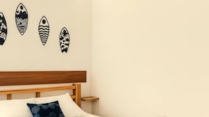 Uma cama com estrutura de madeira, roupa de cama branca e um cobertor estampado em azul escuro.