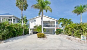 A two-story house with a balcony, surrounded by palm trees and a gravel driveway. - The Sandy Seahorse (Fort Myers Beach)