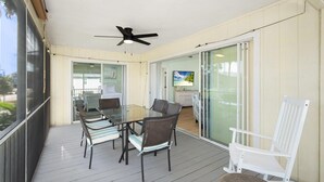 A covered patio with a glass door leading to a kitchen, a dining table with chairs, and a ceiling fan. - The Sandy Seahorse (Fort Myers Beach)