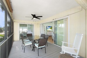 A covered patio with a glass door leading to a kitchen, a dining table with chairs, and a ceiling fan. - The Sandy Seahorse (Fort Myers Beach)